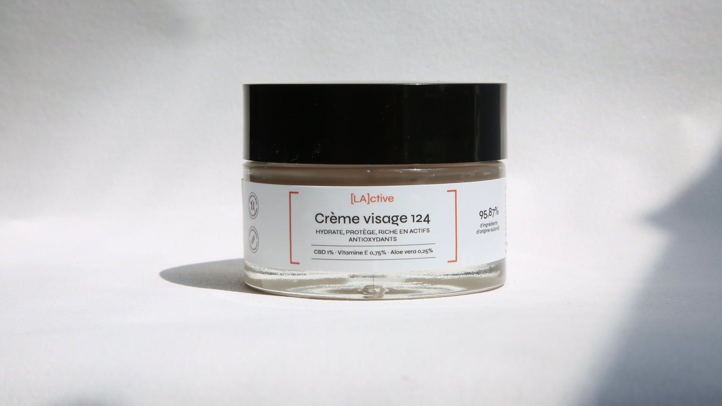 A small jar of face cream labeled “[LA]ctive” with the product name “Face Cream 124”. The jar has a black lid and text indicating that it contains CBD, vitamin E, and aloe vera, but also 95.87% ingredients of natural origin. The jar is set against a plain white background.
