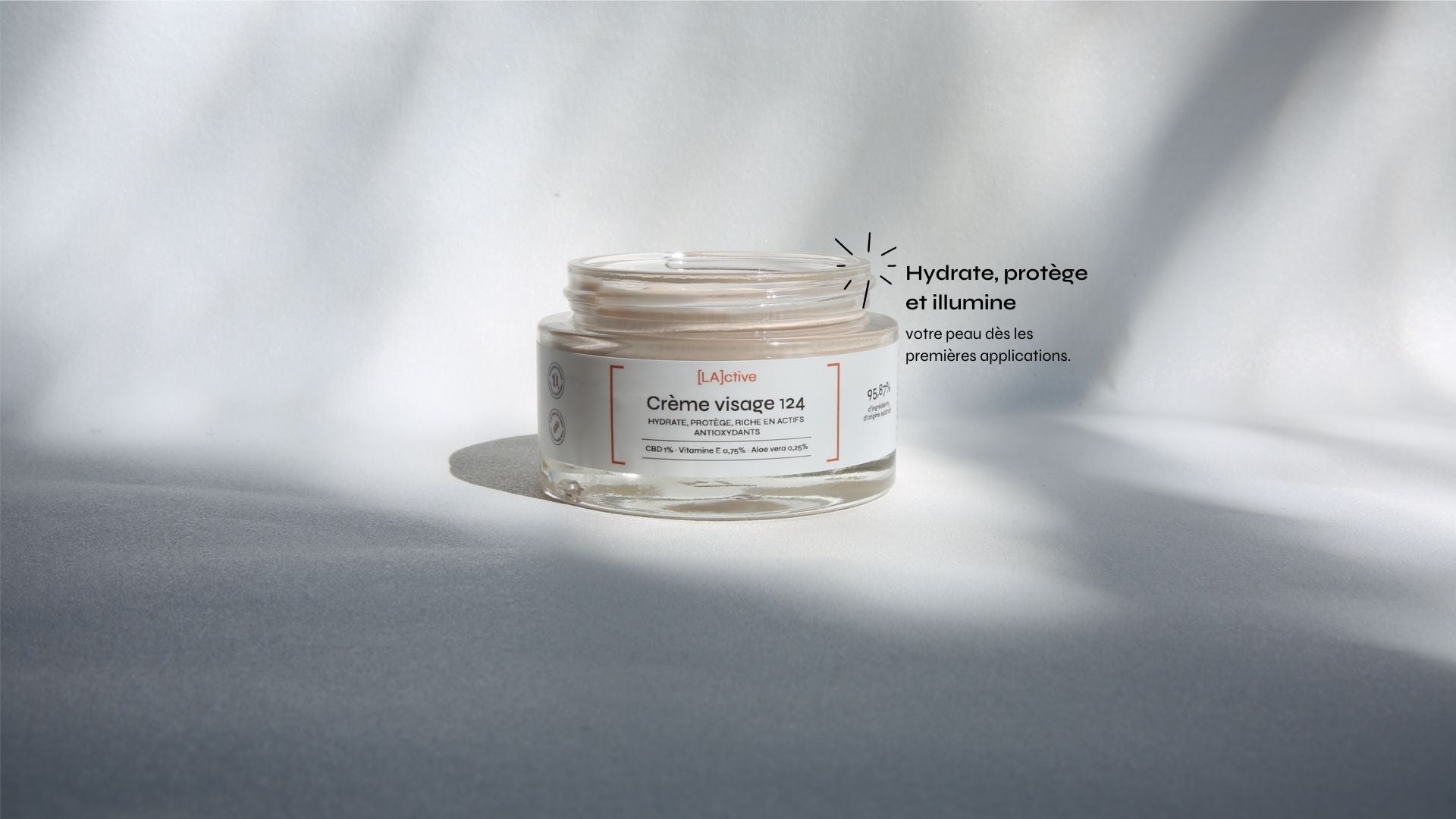 A jar of Crème Visage 124 is placed on a surface, with light casting shadows. French text highlights the cream's hydrating, protective, and illuminating properties.