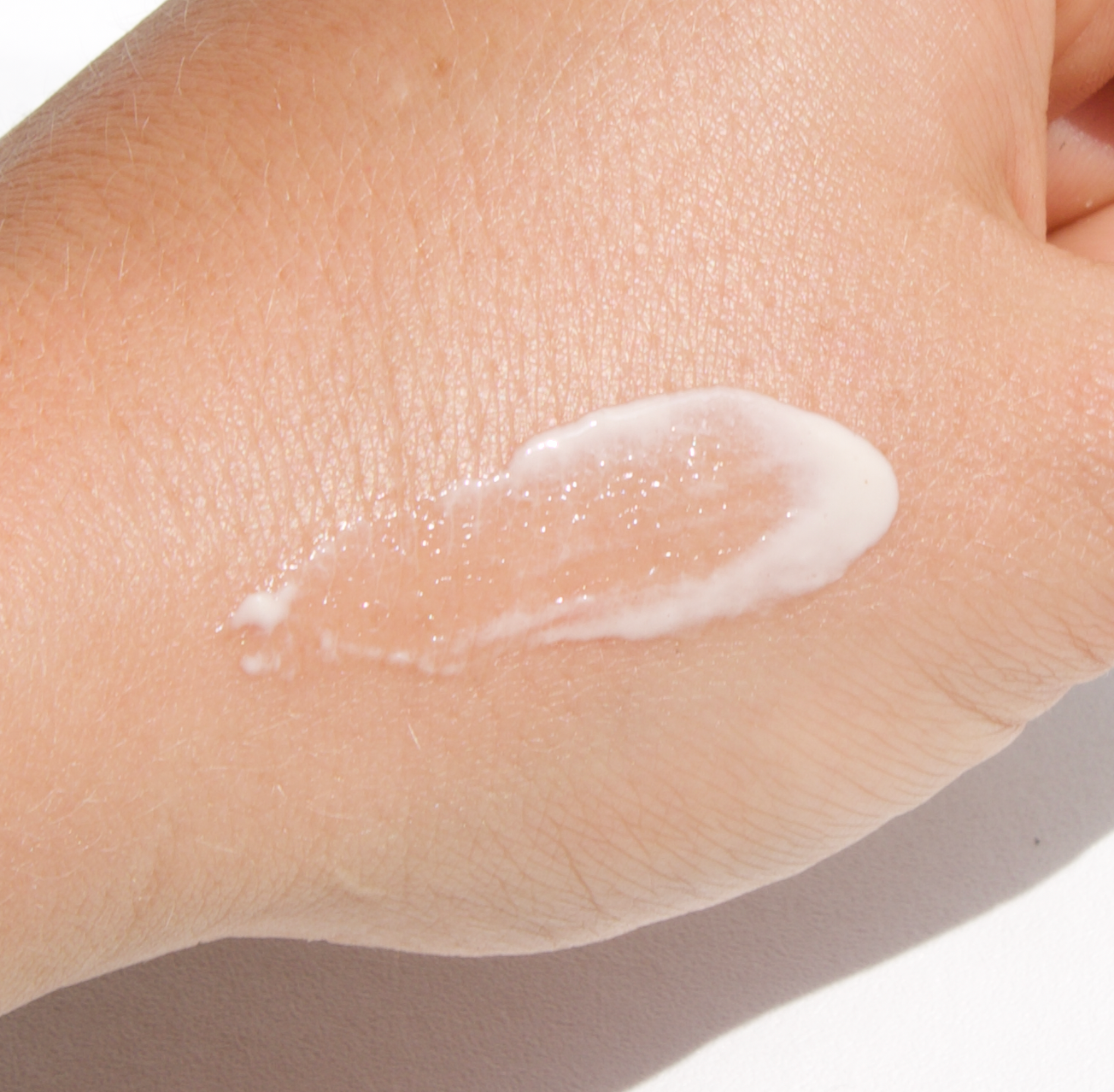 A close-up of a person's hand with a dab of white cream spread across the back of it. The hand is gently resting against a white background.