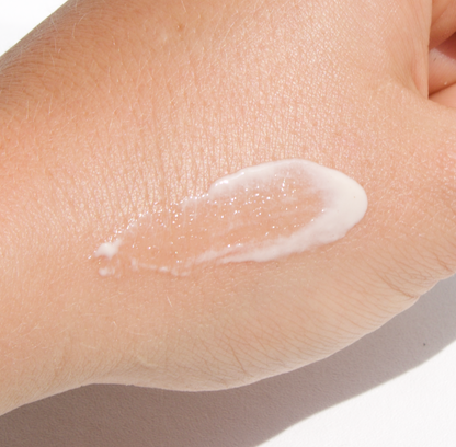 A close-up of a person's hand with a dab of white cream spread across the back of it. The hand is gently resting against a white background.