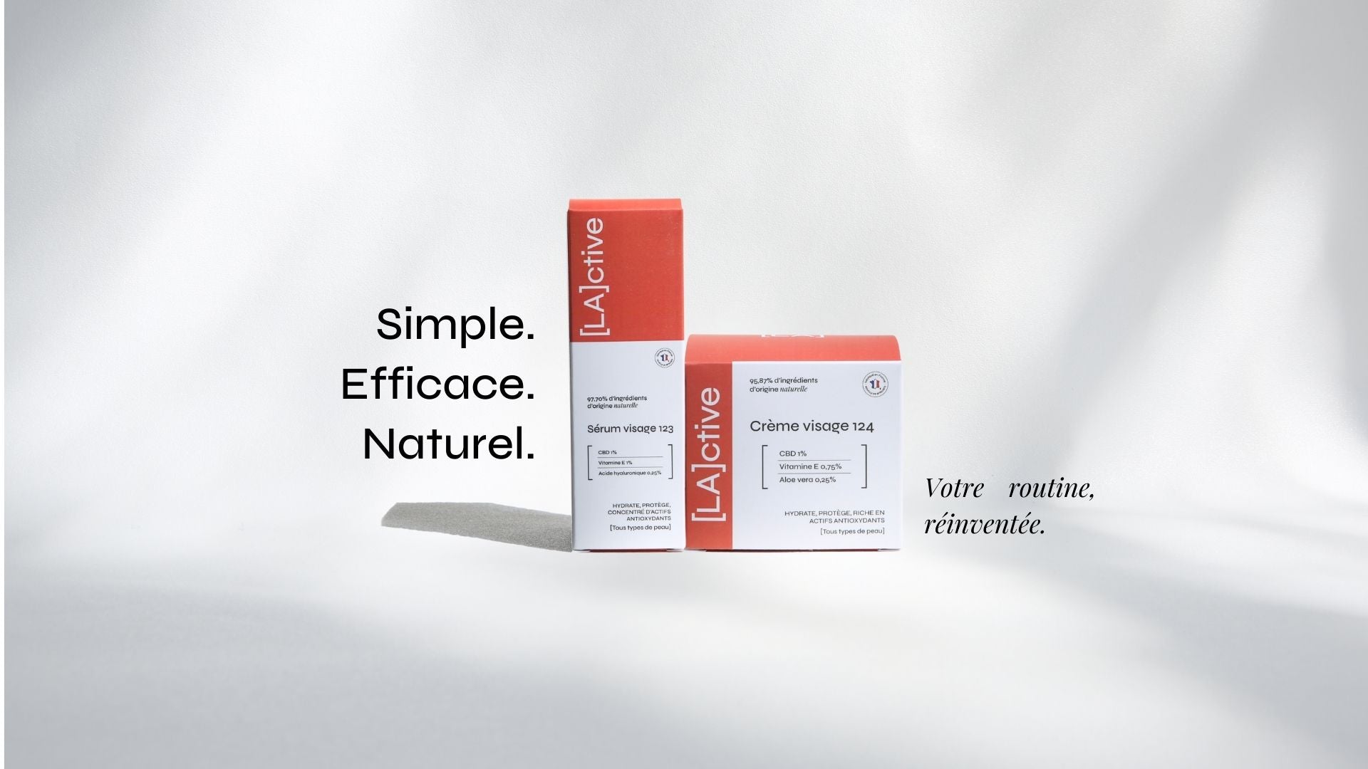 Two boxes of skincare products are displayed against a white backdrop. The packaging is primarily white and orange, labeled "[LA]active." French text reads "Simple. Efficace. Naturelle. Votre routine, réinventée." on the left and right side. Shadows cast softly to the right.