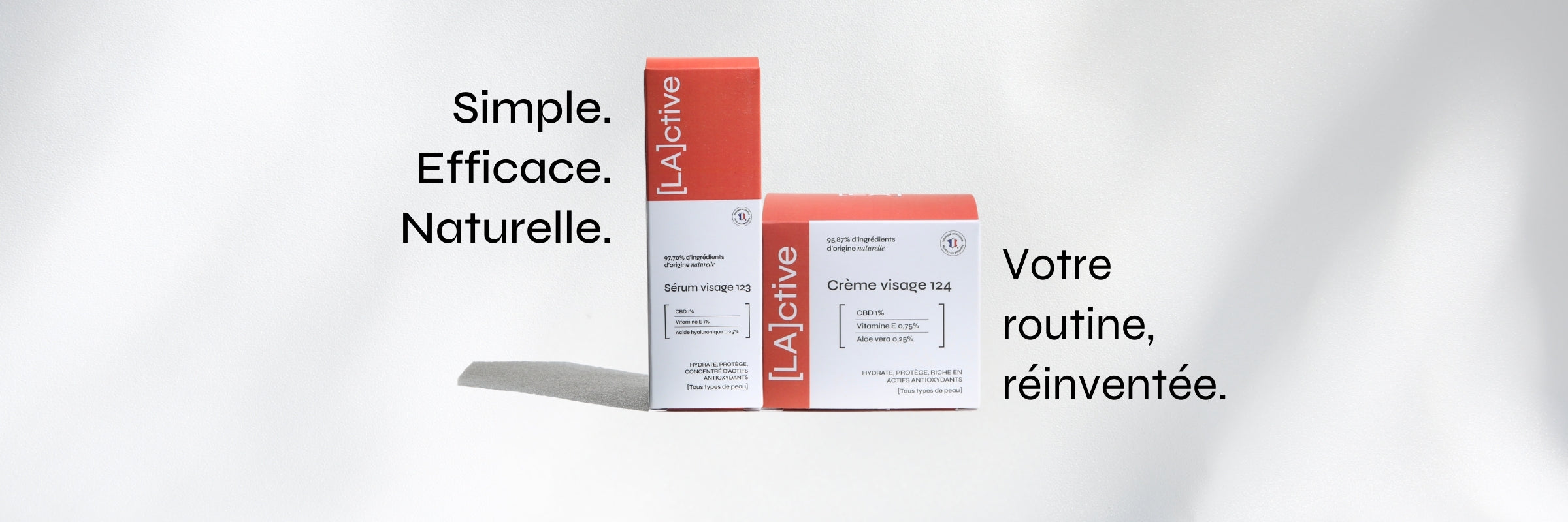 Two boxes of skincare products are displayed against a white backdrop. The packaging is primarily white and orange, labeled "[LA]active." French text reads "Simple. Efficace. Naturelle. Votre routine, réinventée." on the left and right side. Shadows cast softly to the right.